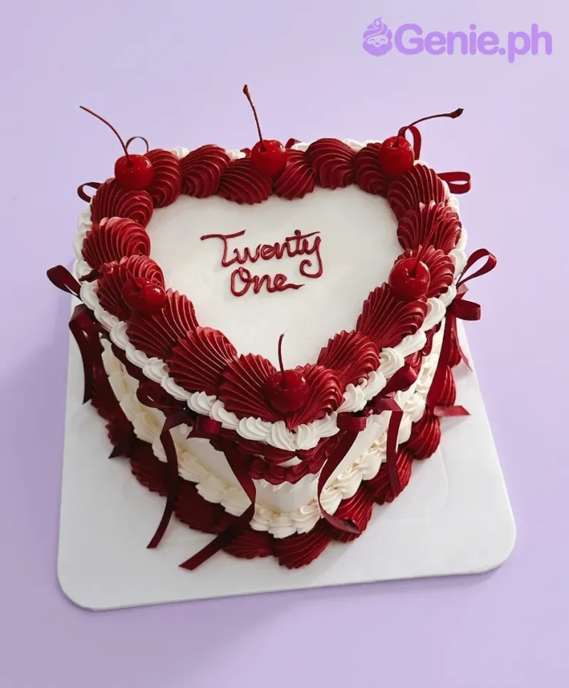 A white and red 1-tier heart-shaped Red Vintage Heart cake, with deep red ruffles, cherries, red ribbons, and 'Twenty One' text. A white and red 1-tier heart-shaped Red Vintage Heart cake, with deep red ruffles, cherries, red ribbons, and 'Twenty One' text.