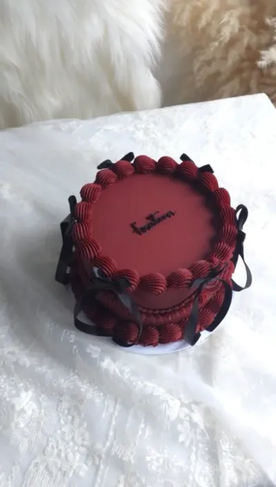 Dark red single-tier round cake with smooth soft icing, black ribbon bows, and piped rosette borders