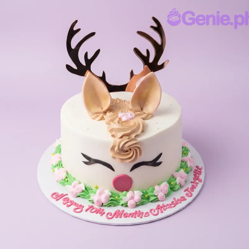 A white 1 Tier Reindeer-themed cake featuring gold antlers, tan ears, red nose, brown icing mane, and pink floral accents. A white 1 Tier Reindeer-themed cake featuring gold antlers, tan ears, red nose, brown icing mane, and pink floral accents.