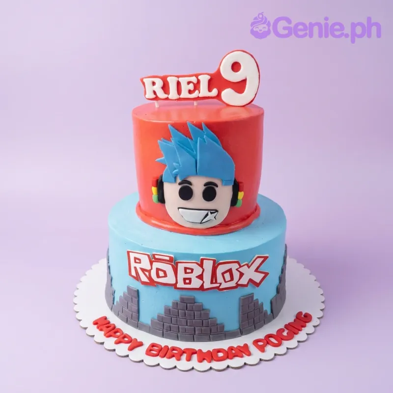 A red and light blue two-tier cake themed around Roblox, featuring a character face, Roblox logo, and grey brick patterns. A red and light blue two-tier cake themed around Roblox, featuring a character face, Roblox logo, and grey brick patterns.