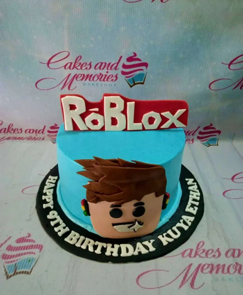 A light blue 1-tier cake themed around Roblox, featuring a large Roblox logo topper and a 3D fondant character face. A light blue 1-tier cake themed around Roblox, featuring a large Roblox logo topper and a 3D fondant character face.