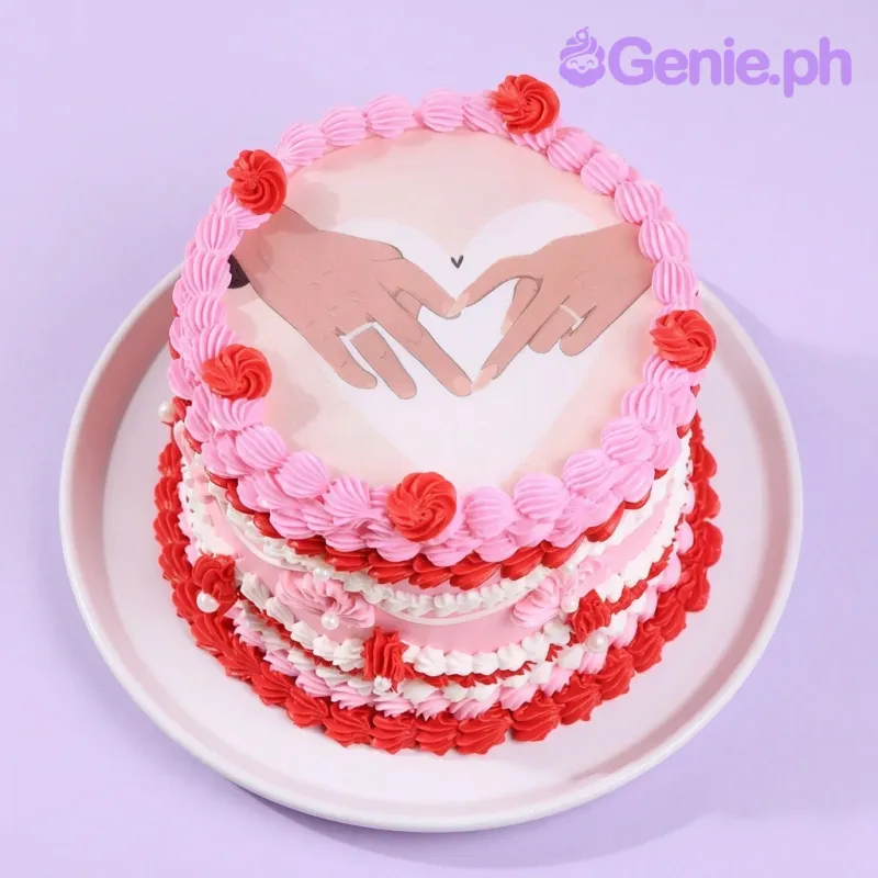 A pink and red 1-tier cake themed Romantic Vintage, featuring a heart-shaped printout of hands and piped icing ruffles. A pink and red 1-tier cake themed Romantic Vintage, featuring a heart-shaped printout of hands and piped icing ruffles.