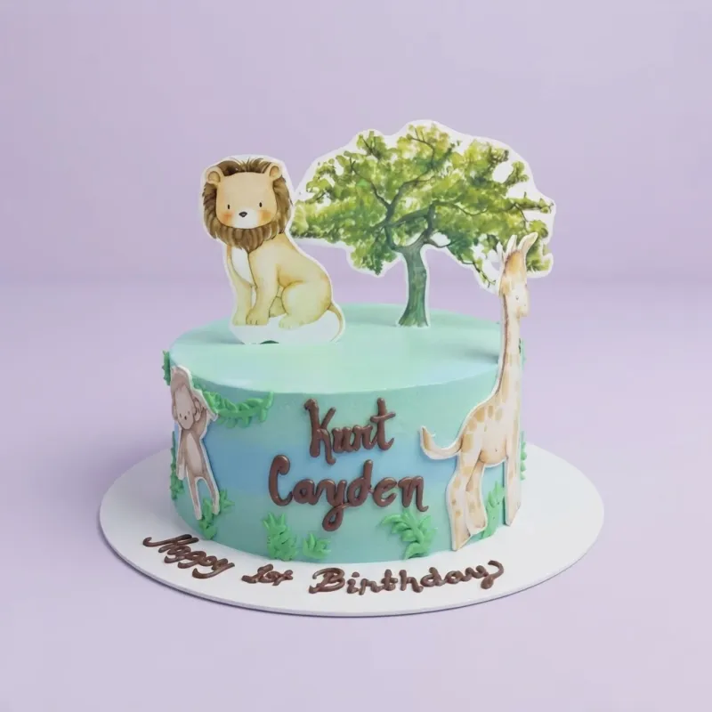 A light blue 1 Tier cake, Safari Lion themed, with lion, giraffe, tree, and monkey printouts, plus piped green icing grass. A light blue 1 Tier cake, Safari Lion themed, with lion, giraffe, tree, and monkey printouts, plus piped green icing grass.