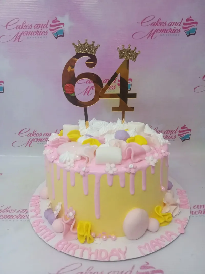 A yellow and pink 1-tier Senior Birthday cake, featuring gold 64 toppers with crowns and white swirls. A yellow and pink 1-tier Senior Birthday cake, featuring gold 64 toppers with crowns and white swirls.