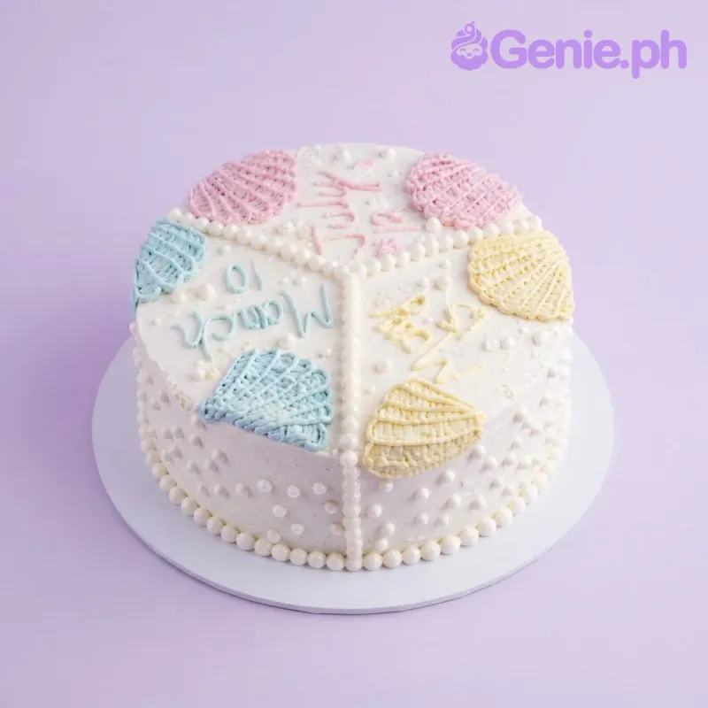 White round cake with pastel piped shell decorations and handwritten dates in icing White round cake with pastel piped shell decorations and handwritten dates in icing