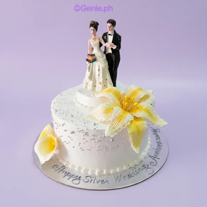 A white 1-tier cake themed for a Silver Anniversary, featuring a bride and groom topper, yellow lilies, and silver dragees. A white 1-tier cake themed for a Silver Anniversary, featuring a bride and groom topper, yellow lilies, and silver dragees.