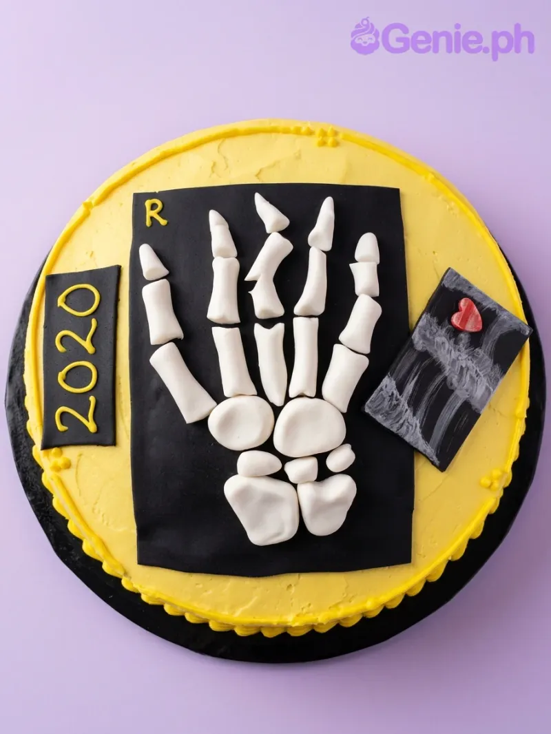 A yellow 1-tier round cake themed around Skeleton X-Ray, featuring a 3D fondant skeleton hand, a black X-ray panel, and "2020" text. A yellow 1-tier round cake themed around Skeleton X-Ray, featuring a 3D fondant skeleton hand, a black X-ray panel, and "2020" text.
