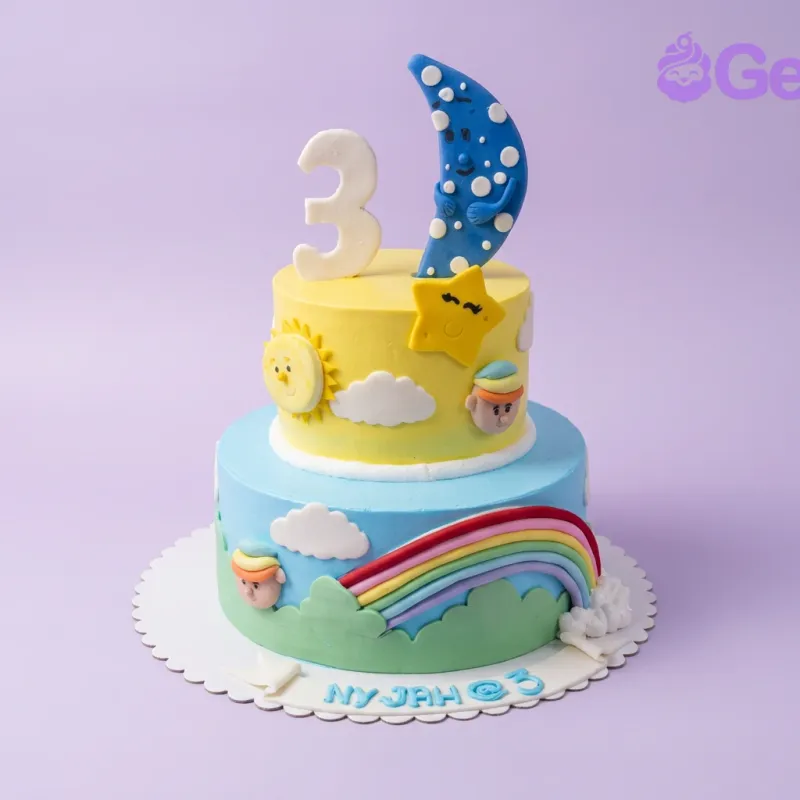 A yellow and blue two-tier cake themed around the sky, featuring a crescent moon, a number three, a sun, stars, and a rainbow. A yellow and blue two-tier cake themed around the sky, featuring a crescent moon, a number three, a sun, stars, and a rainbow.