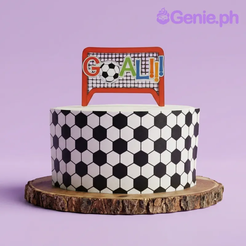 A white and black 1-tier cake, soccer-themed, featuring a soccer goal and "GOAL" topper with a hexagon pattern wrap. A white and black 1-tier cake, soccer-themed, featuring a soccer goal and "GOAL" topper with a hexagon pattern wrap.