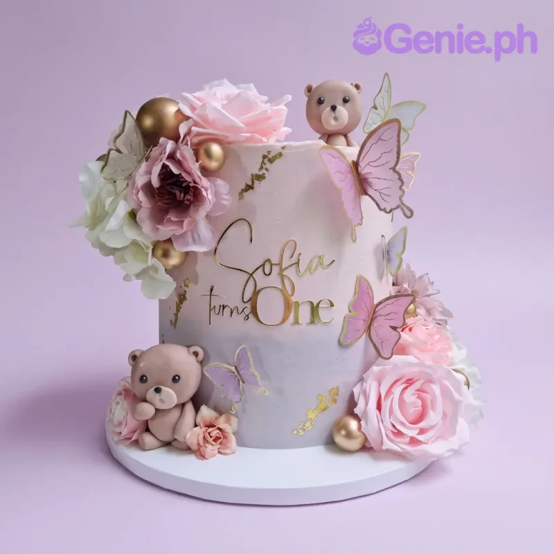 A pink and purple 1-tier Sofia First Birthday cake with fondant bears, roses, gold spheres, and butterflies. A pink and purple 1-tier Sofia First Birthday cake with fondant bears, roses, gold spheres, and butterflies.