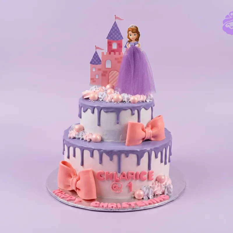 A white and purple two-tier cake themed around Sofia The First, featuring castle and Sofia character, with pink bows and silver beads. A white and purple two-tier cake themed around Sofia The First, featuring castle and Sofia character, with pink bows and silver beads.