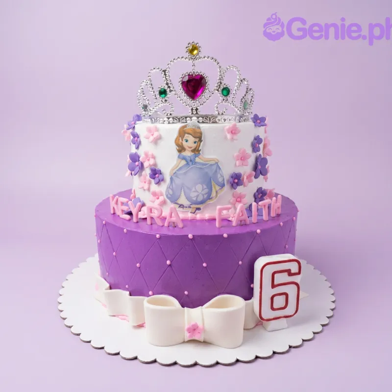A purple and white two-tier cake themed Sofia The First, featuring a silver tiara, character printout, and pink and purple flowers. A purple and white two-tier cake themed Sofia The First, featuring a silver tiara, character printout, and pink and purple flowers.