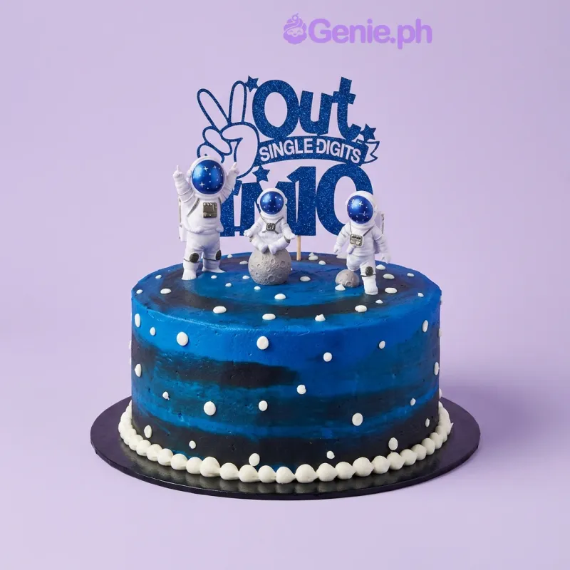 Blue and black gradient soft-iced 1-tier cake with three astronaut figurines, an 'Out of this world' text topper, moon spheres, and piped white dots Blue and black gradient soft-iced 1-tier cake with three astronaut figurines, an 'Out of this world' text topper, moon spheres, and piped white dots