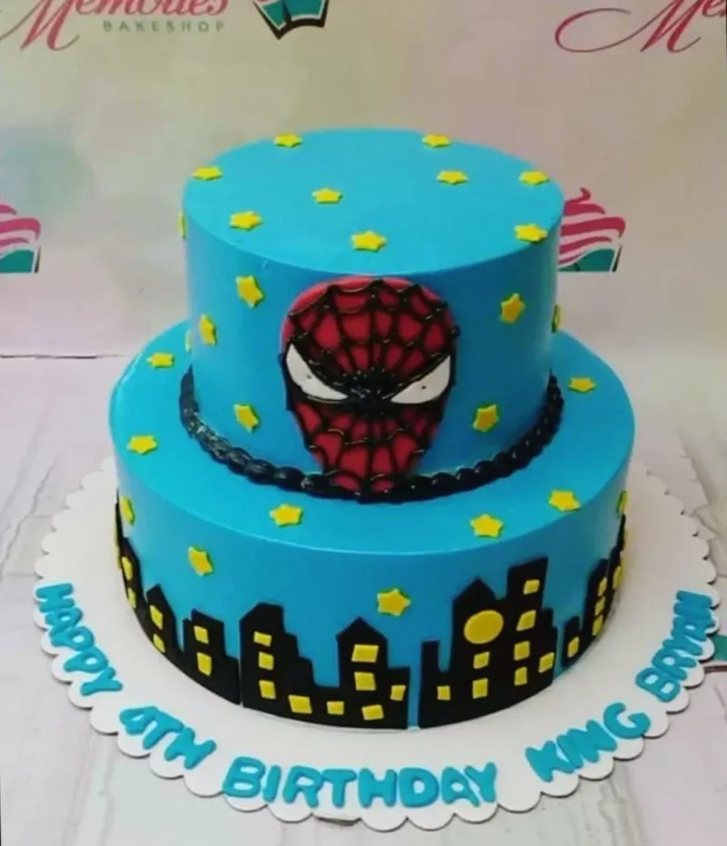 A blue 2-tier cake themed around Spiderman, featuring a fondant Spiderman mask, city skyline silhouette, and yellow stars. A blue 2-tier cake themed around Spiderman, featuring a fondant Spiderman mask, city skyline silhouette, and yellow stars.