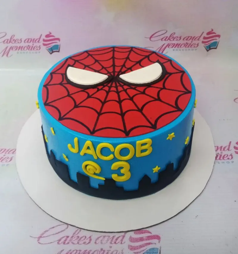 A red and blue 1-tier cake themed around Spiderman, featuring white eyes, a black city skyline, yellow stars, and a black spider web. A red and blue 1-tier cake themed around Spiderman, featuring white eyes, a black city skyline, yellow stars, and a black spider web.