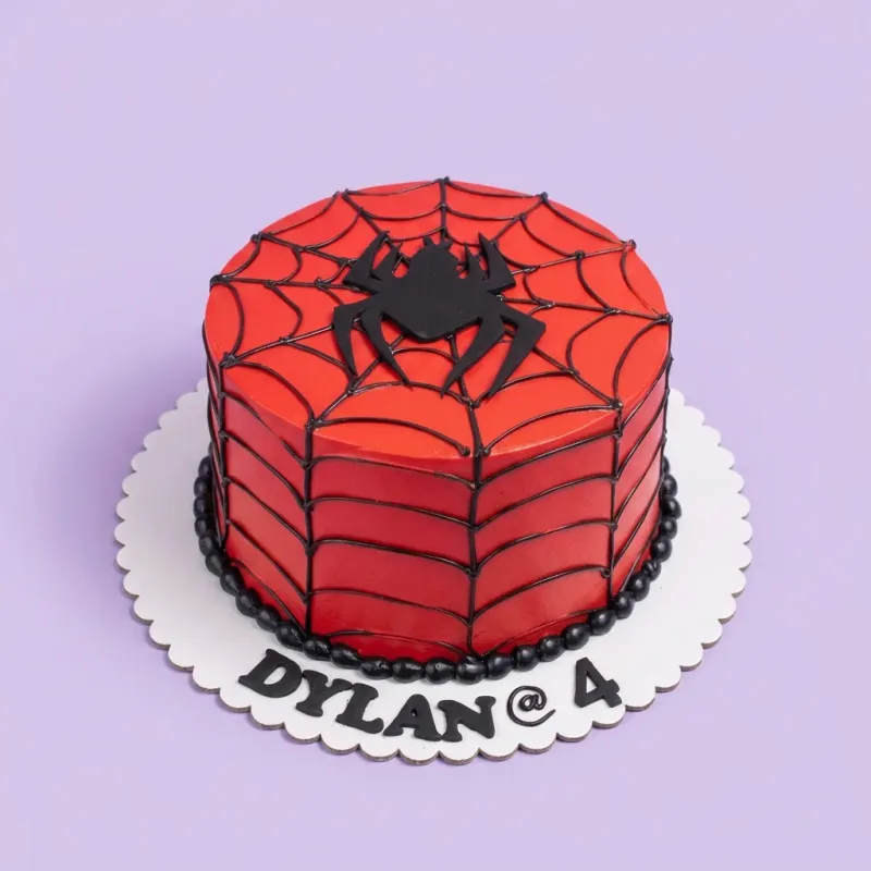 A red, black, and white 1 Tier cake themed around Spiderman, featuring a black spider topper, black spider web icing, and 'DYLAN @ 4' text. A red, black, and white 1 Tier cake themed around Spiderman, featuring a black spider topper, black spider web icing, and 'DYLAN @ 4' text.