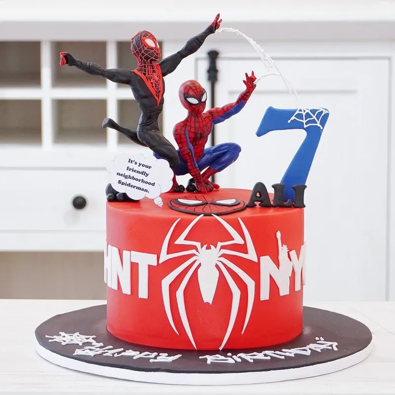 Red 1-tier fondant Spiderman birthday cake with two action figures, number seven topper, and white web accents Red 1-tier fondant Spiderman birthday cake with two action figures, number seven topper, and white web accents
