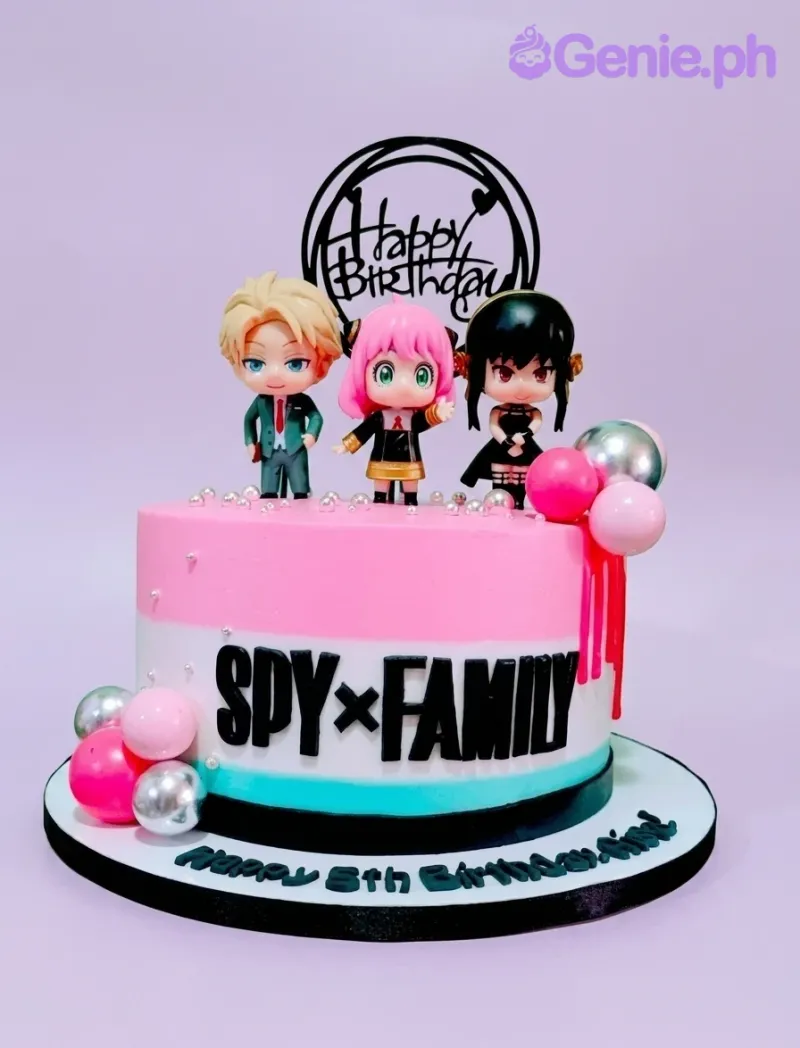 A pink and white 1-tier Spy X Family cake with Loid, Anya, Yor figurines, a 'Happy Birthday' topper, and silver pearl accents. A pink and white 1-tier Spy X Family cake with Loid, Anya, Yor figurines, a 'Happy Birthday' topper, and silver pearl accents.