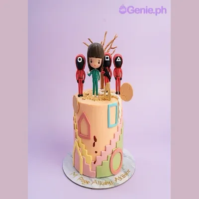Peach fondant cake with Squid Game character toppers and geometric side decorations Peach fondant cake with Squid Game character toppers and geometric side decorations