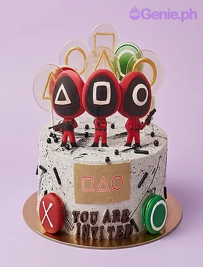 Squid Game cake design — 1 layer soft icing cake in white — with Squid Game guard characters, translucent gold and green discs, red and green macarons, gold panel with geometric shapes, and custom "YOU ARE INVITED" message Squid Game cake design — 1 layer soft icing cake in white — with Squid Game guard characters, translucent gold and green discs, red and green macarons, gold panel with geometric shapes, and custom "YOU ARE INVITED" message