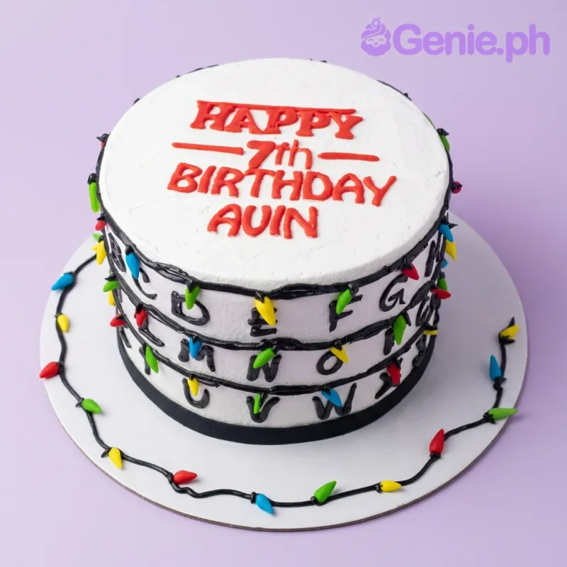 A white 1 Tier cake themed around Stranger Things, featuring red text, black wire piping, colorful light bulbs, and black alphabet letters. A white 1 Tier cake themed around Stranger Things, featuring red text, black wire piping, colorful light bulbs, and black alphabet letters.