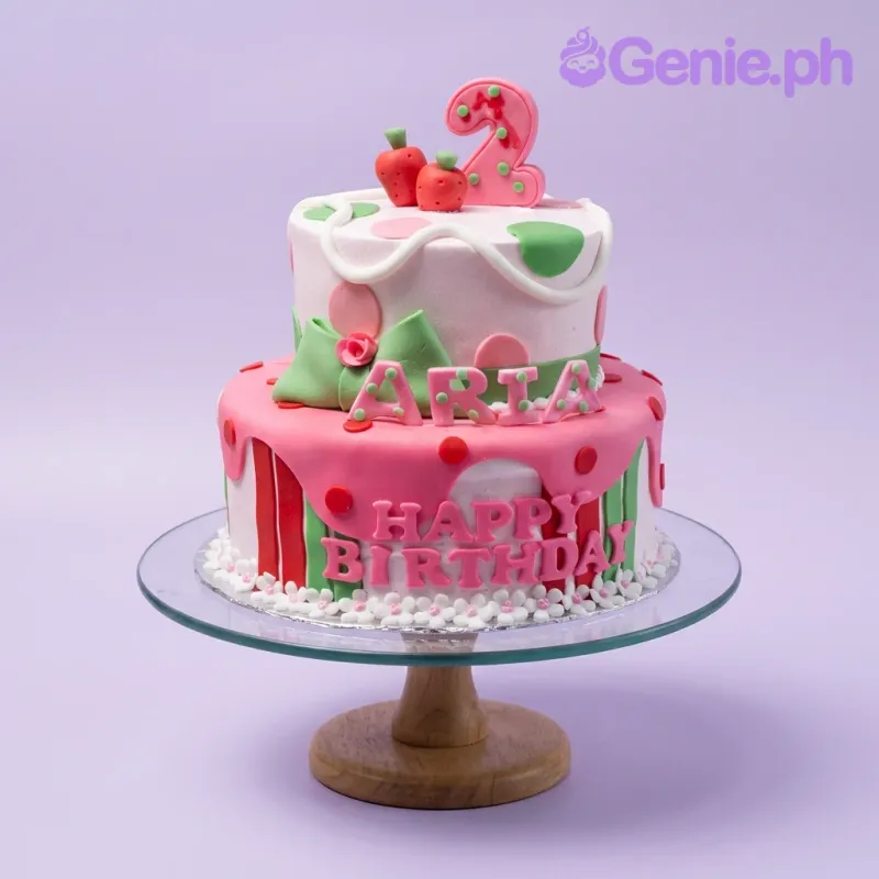 A pink and white two-tier fondant cake, Strawberry Birthday themed, with a large pink number two and fondant strawberries. A pink and white two-tier fondant cake, Strawberry Birthday themed, with a large pink number two and fondant strawberries.