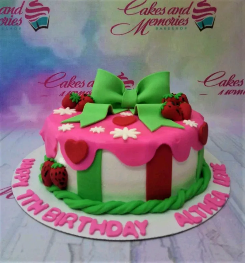A pink, white, green, and red 1 Tier Fondant strawberry cake, featuring a large green bow, 3D strawberries, and red hearts. A pink, white, green, and red 1 Tier Fondant strawberry cake, featuring a large green bow, 3D strawberries, and red hearts.