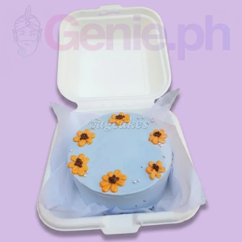 A light blue bento cake themed around sunflowers, featuring orange piped icing sunflowers and silver dragees. A light blue bento cake themed around sunflowers, featuring orange piped icing sunflowers and silver dragees.