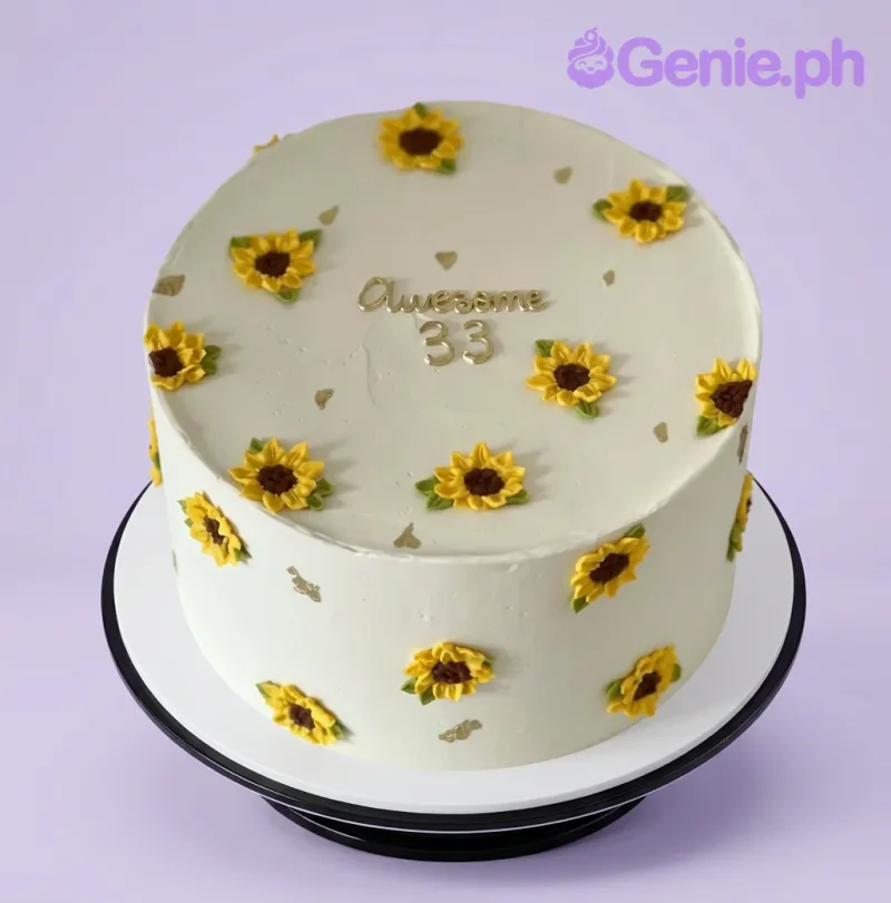 A white 1-tier Sunflower Minimalist cake with yellow piped sunflowers, gold 'Awesome 33' text, and gold leaf accents. A white 1-tier Sunflower Minimalist cake with yellow piped sunflowers, gold 'Awesome 33' text, and gold leaf accents.