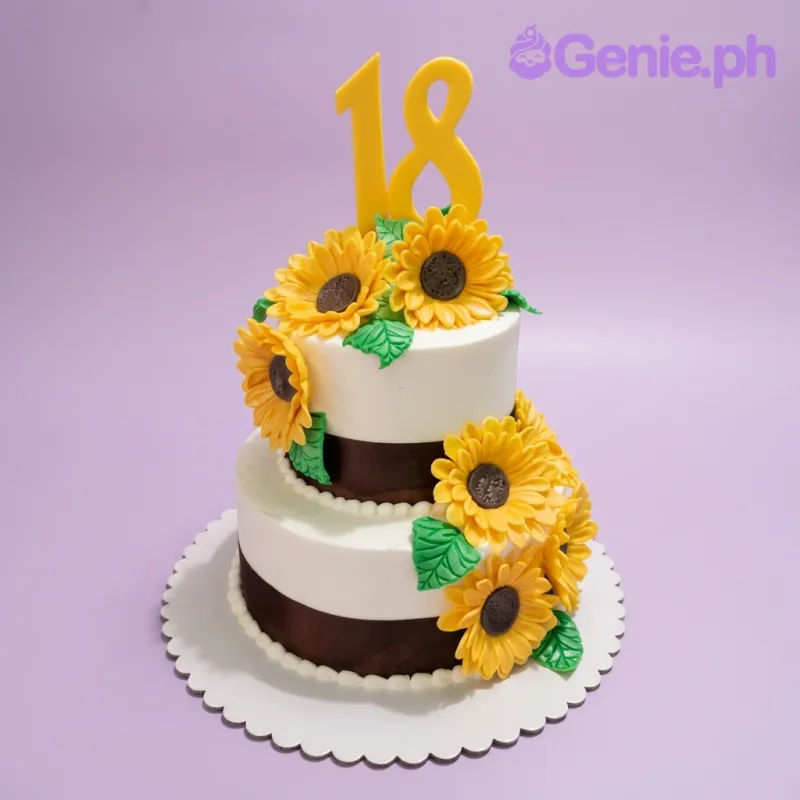 Two-tier white sunflower birthday cake with yellow number 18 topper and brown ribbon accents. Two-tier white sunflower birthday cake with yellow number 18 topper and brown ribbon accents.