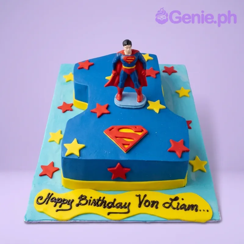 A blue number one shaped cake themed around Superman, featuring a Superman figurine, red and yellow stars, and a Superman logo. A blue number one shaped cake themed around Superman, featuring a Superman figurine, red and yellow stars, and a Superman logo.