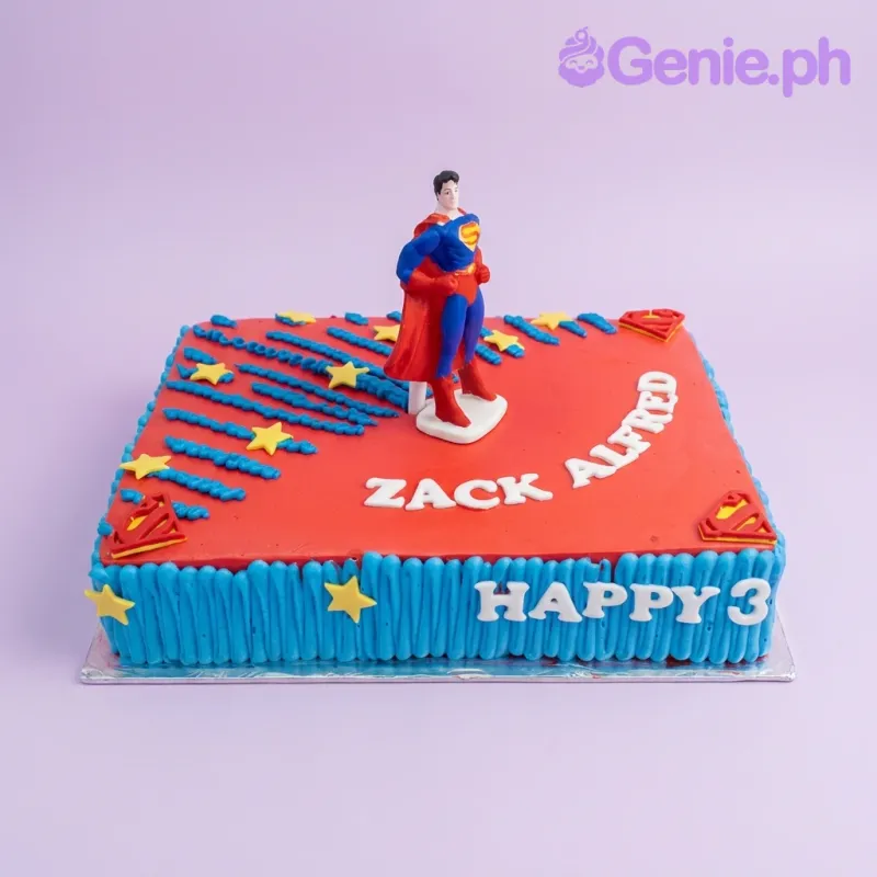 A red and blue rectangle cake themed around Superman, featuring a Superman figurine, yellow stars, and text. A red and blue rectangle cake themed around Superman, featuring a Superman figurine, yellow stars, and text.