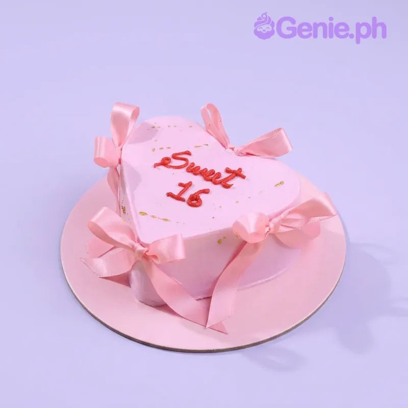 Pink heart-shaped cake with smooth soft icing, red piped text, and pink satin ribbon bows Pink heart-shaped cake with smooth soft icing, red piped text, and pink satin ribbon bows