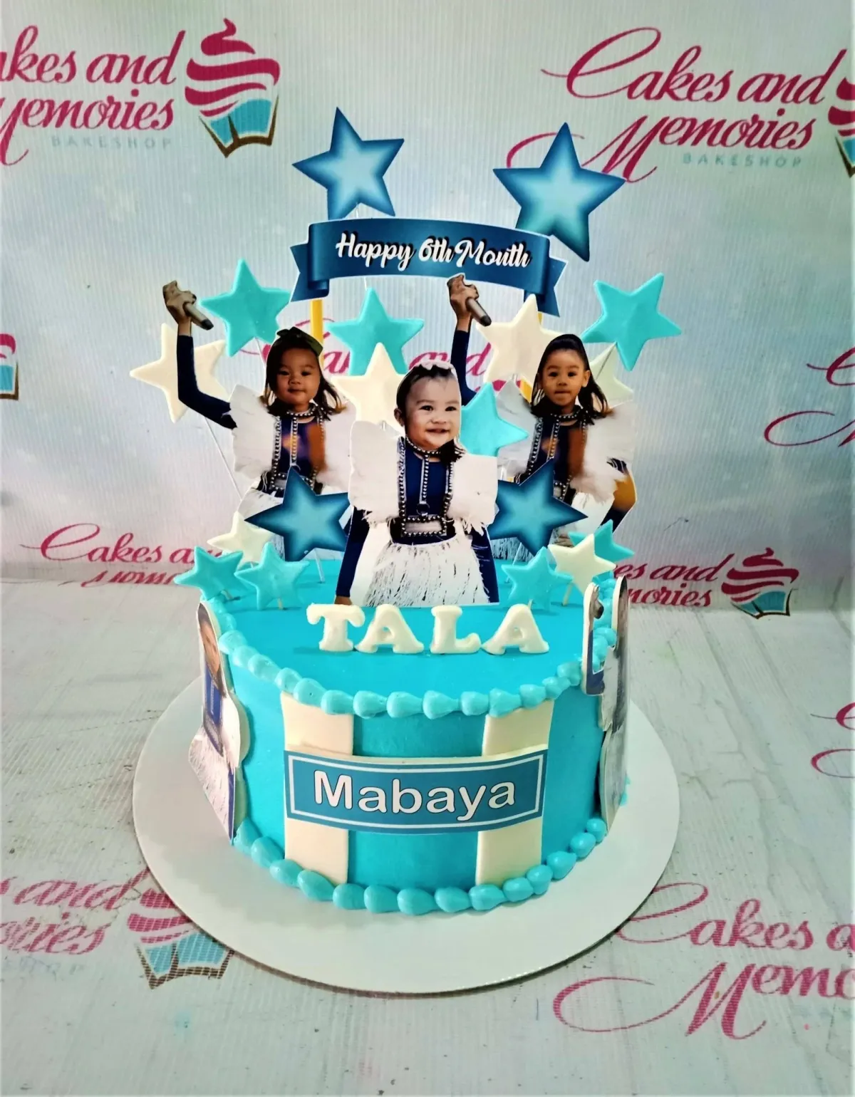 A light blue 1 Tier cake for Tala Mabaya's 6th Month, featuring baby photos, a "Happy 6th Month" banner, and stars. A light blue 1 Tier cake for Tala Mabaya's 6th Month, featuring baby photos, a "Happy 6th Month" banner, and stars.