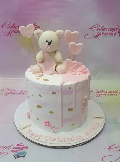 White and pink 1-tier christening cake with a large fondant teddy bear topper, pink hearts, and gold paint splatters. White and pink 1-tier christening cake with a large fondant teddy bear topper, pink hearts, and gold paint splatters.