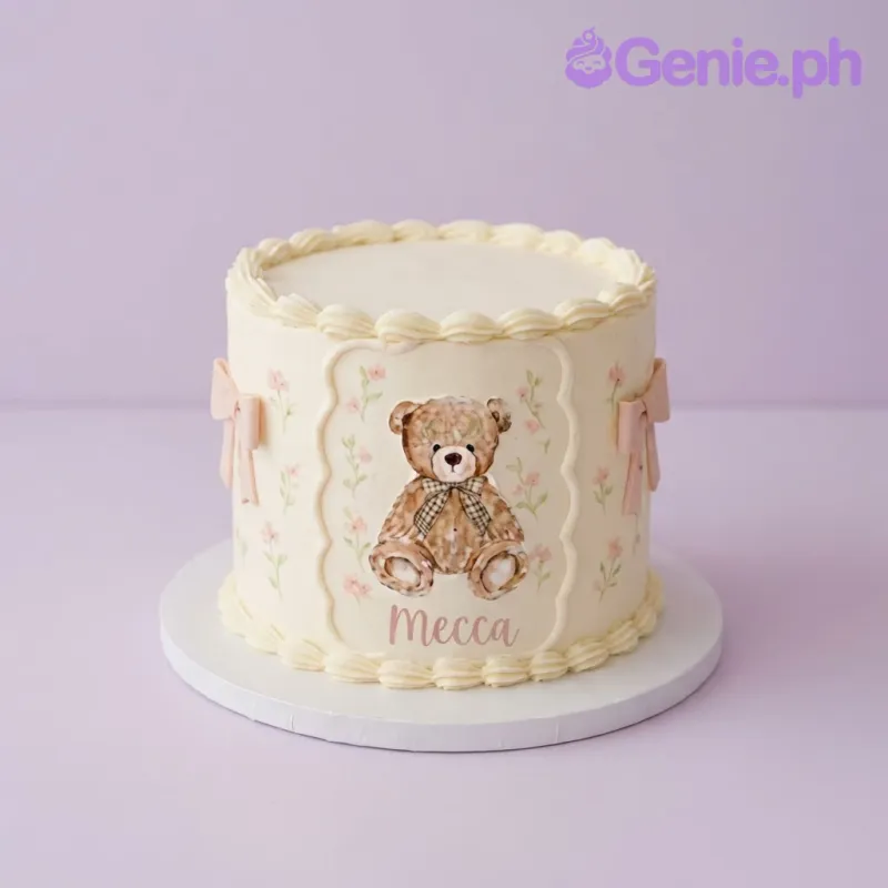 Ivory 1-tier soft icing cake with a printed teddy bear plaque, pink ribbon bows, and piped borders Ivory 1-tier soft icing cake with a printed teddy bear plaque, pink ribbon bows, and piped borders