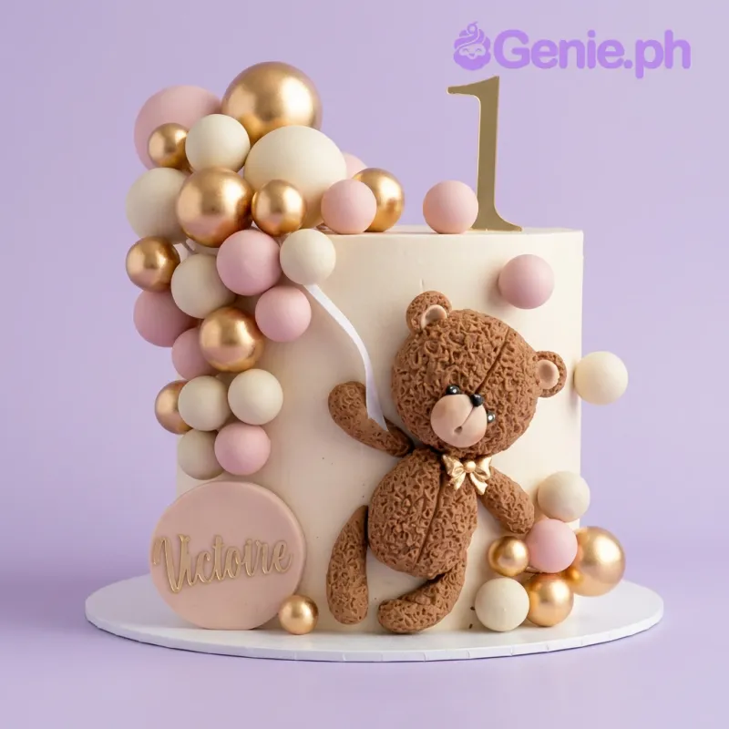 Ivory 1-tier birthday cake with a brown fondant teddy bear, gold number 1 topper, and a cluster of pink, white, and gold balloons Ivory 1-tier birthday cake with a brown fondant teddy bear, gold number 1 topper, and a cluster of pink, white, and gold balloons