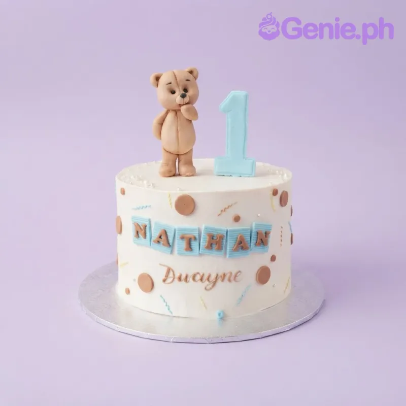 White 1-tier birthday cake with smooth soft icing, a teddy bear topper, number one, and blue name plaques White 1-tier birthday cake with smooth soft icing, a teddy bear topper, number one, and blue name plaques