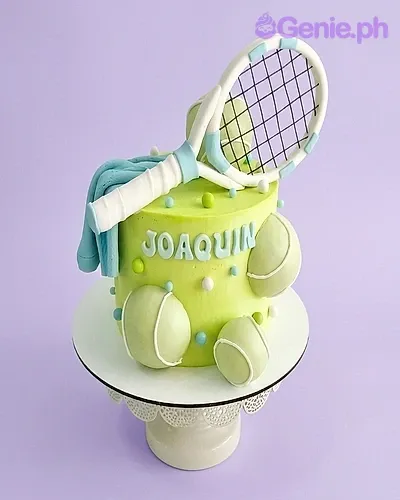 A light green 1-tier cake themed around Tennis, featuring a large fondant tennis racket, tennis balls, blue gumpaste letters, and decorative dots. A light green 1-tier cake themed around Tennis, featuring a large fondant tennis racket, tennis balls, blue gumpaste letters, and decorative dots.