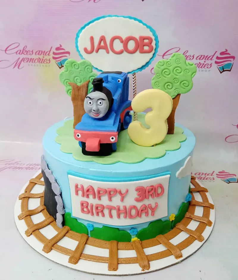Thomas the Tank Engine themed blue fondant cake with a 3D train topper, gumpaste trees, and a train track on the base board. Thomas the Tank Engine themed blue fondant cake with a 3D train topper, gumpaste trees, and a train track on the base board.