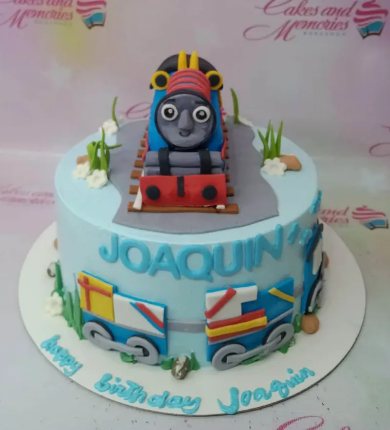 Light blue Thomas the Tank Engine themed birthday cake with a 3D fondant train on tracks and side decorations. Light blue Thomas the Tank Engine themed birthday cake with a 3D fondant train on tracks and side decorations.