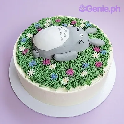A white 1-tier round cake themed around Totoro, featuring a 3D fondant Totoro figure on green piped grass with colorful flowers. A white 1-tier round cake themed around Totoro, featuring a 3D fondant Totoro figure on green piped grass with colorful flowers.