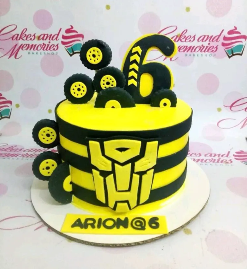 A yellow and black 1 Tier cake themed around Transformers Bumblebee, featuring a number six topper, Transformers logo, and fondant tires. A yellow and black 1 Tier cake themed around Transformers Bumblebee, featuring a number six topper, Transformers logo, and fondant tires.