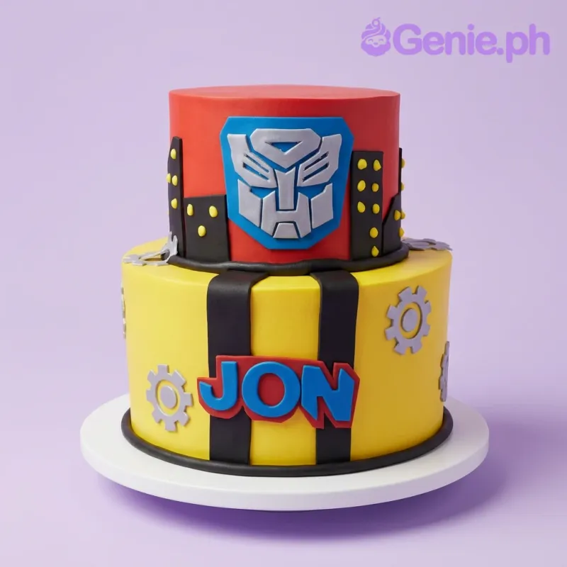 A red and yellow two-tier fondant Transformers cake with an Autobot logo, black stripes, grey gears, and 'JON'. A red and yellow two-tier fondant Transformers cake with an Autobot logo, black stripes, grey gears, and 'JON'.