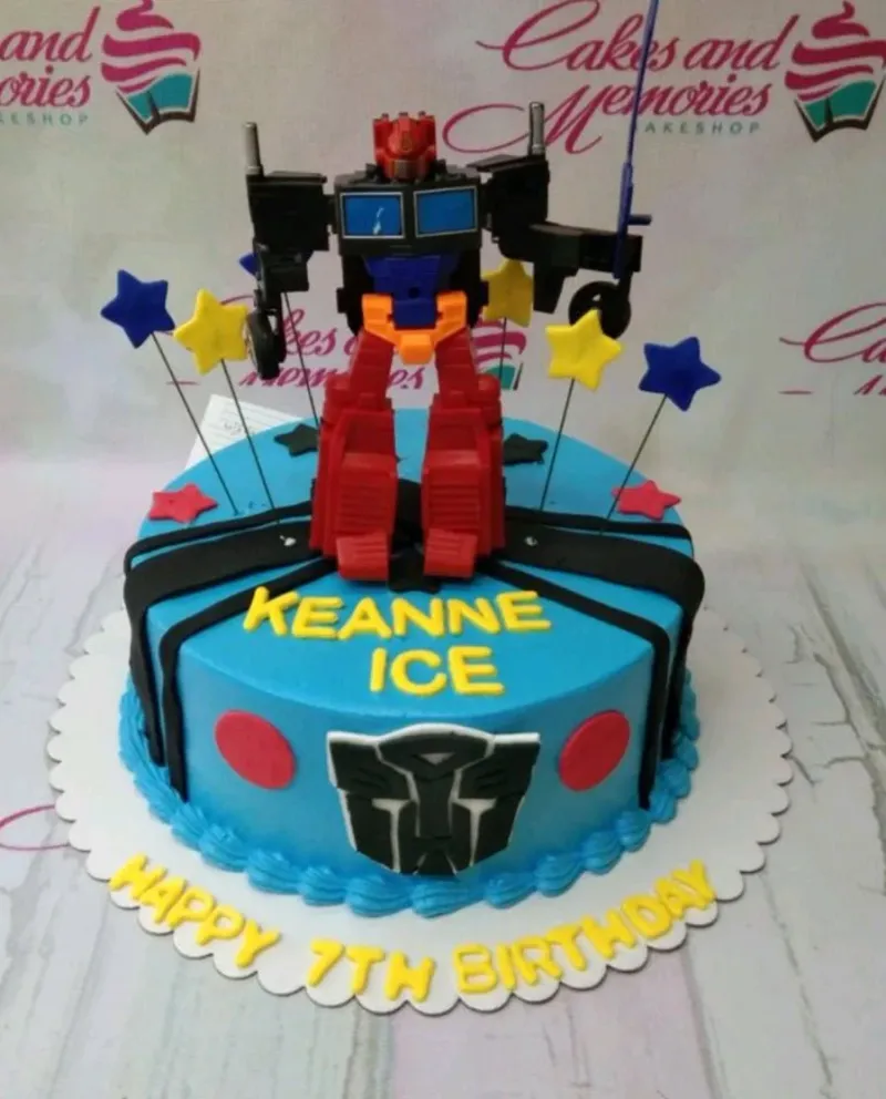 A blue and colorful 1 Tier cake themed around Transformers, featuring a large Optimus Prime toy and fondant stars. A blue and colorful 1 Tier cake themed around Transformers, featuring a large Optimus Prime toy and fondant stars.