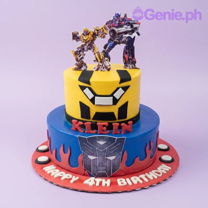 A blue, yellow, and red 2-tier fondant cake themed around Transformers, featuring Bumblebee and Optimus Prime cutouts. A blue, yellow, and red 2-tier fondant cake themed around Transformers, featuring Bumblebee and Optimus Prime cutouts.