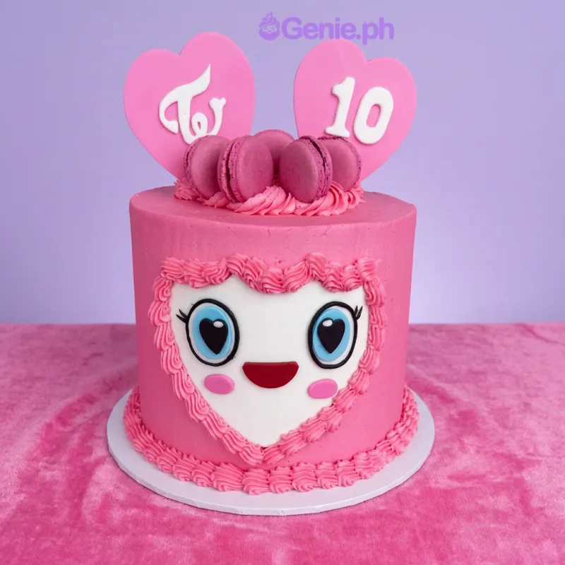 Light pink 1-tier cake with Twice Kpop heart logo toppers, pink macarons, and a heart-shaped face panel with edible features Light pink 1-tier cake with Twice Kpop heart logo toppers, pink macarons, and a heart-shaped face panel with edible features