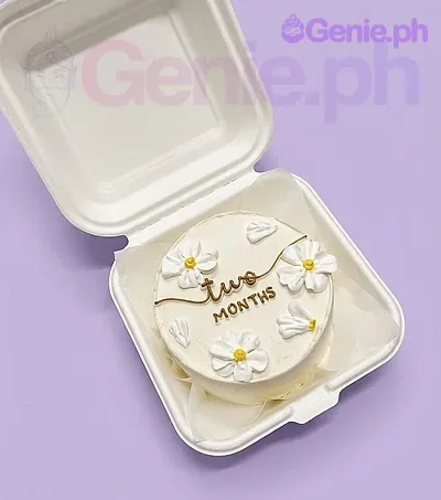 A white Bento cake themed for a Two Months celebration, featuring piped white icing daisies with yellow centers and a 'two MONTHS' message. A white Bento cake themed for a Two Months celebration, featuring piped white icing daisies with yellow centers and a 'two MONTHS' message.