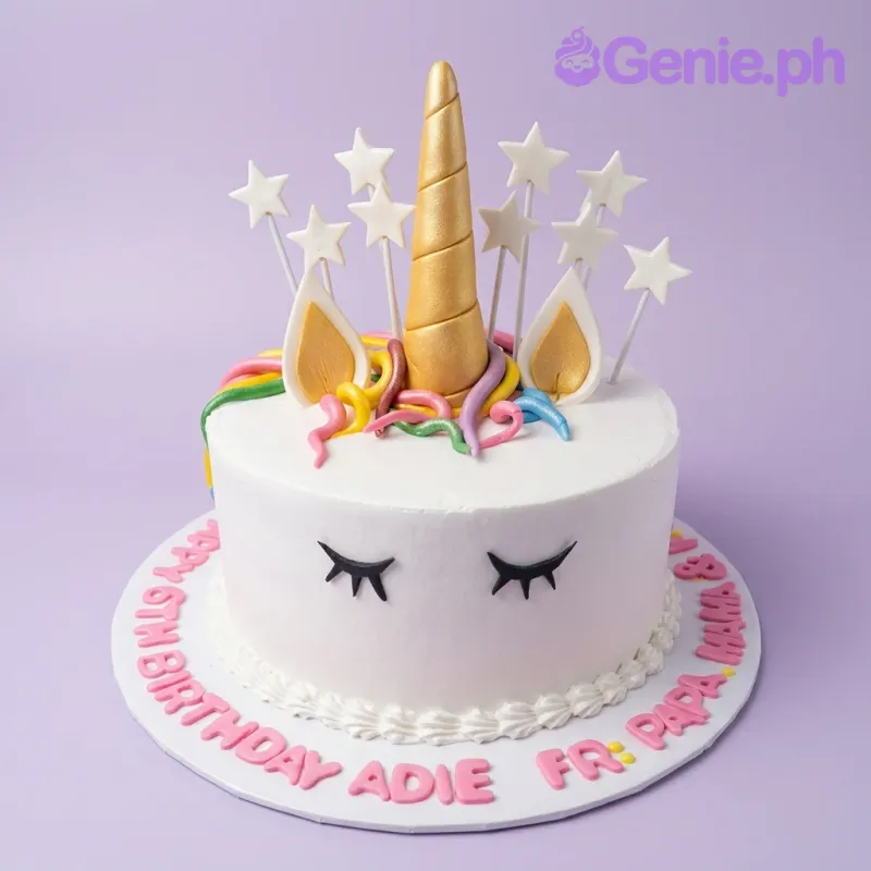 A white 1-tier cake themed around Unicorn, featuring a gold horn, white ears, colorful fondant mane, white star toppers, and a pink message board. A white 1-tier cake themed around Unicorn, featuring a gold horn, white ears, colorful fondant mane, white star toppers, and a pink message board.
