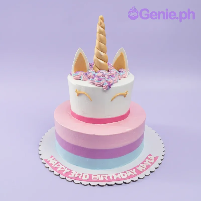 A white, pink, purple, blue, and gold 2-tier Unicorn cake, featuring a gold horn and ears, with a striped base and colorful icing rosettes. A white, pink, purple, blue, and gold 2-tier Unicorn cake, featuring a gold horn and ears, with a striped base and colorful icing rosettes.